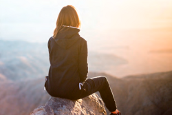 Jugendliche auf Fels sitzend im Gegenlicht